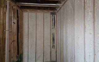 Open-cell spray polyurethane foam insulation on hallway nook walls with plumbing lines.