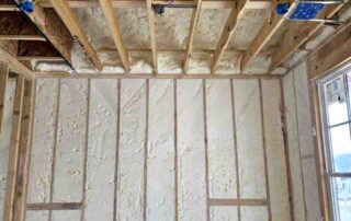Open-cell spray polyurethane foam insulation on garage ceiling joists and exterior wall studs near window.