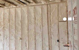 Open-cell spray polyurethane foam insulation on ceiling joists and wall studs.