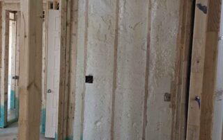 Open-cell spray polyurethane foam insulation in closet alcove wall framing near hallway door.
