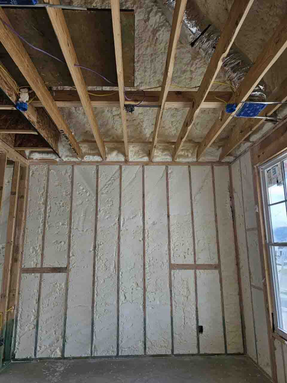 Open-cell spray polyurethane foam insulation on garage ceiling joists and exterior wall studs near window by Hayes Insulation at 3322 Fulmar Circle, Frisco, TX.