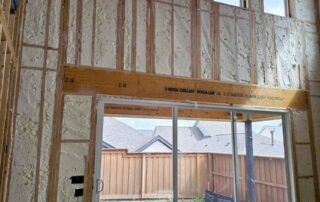 Open-cell spray polyurethane foam insulation on two-story wall with upper windows above sliding glass door.